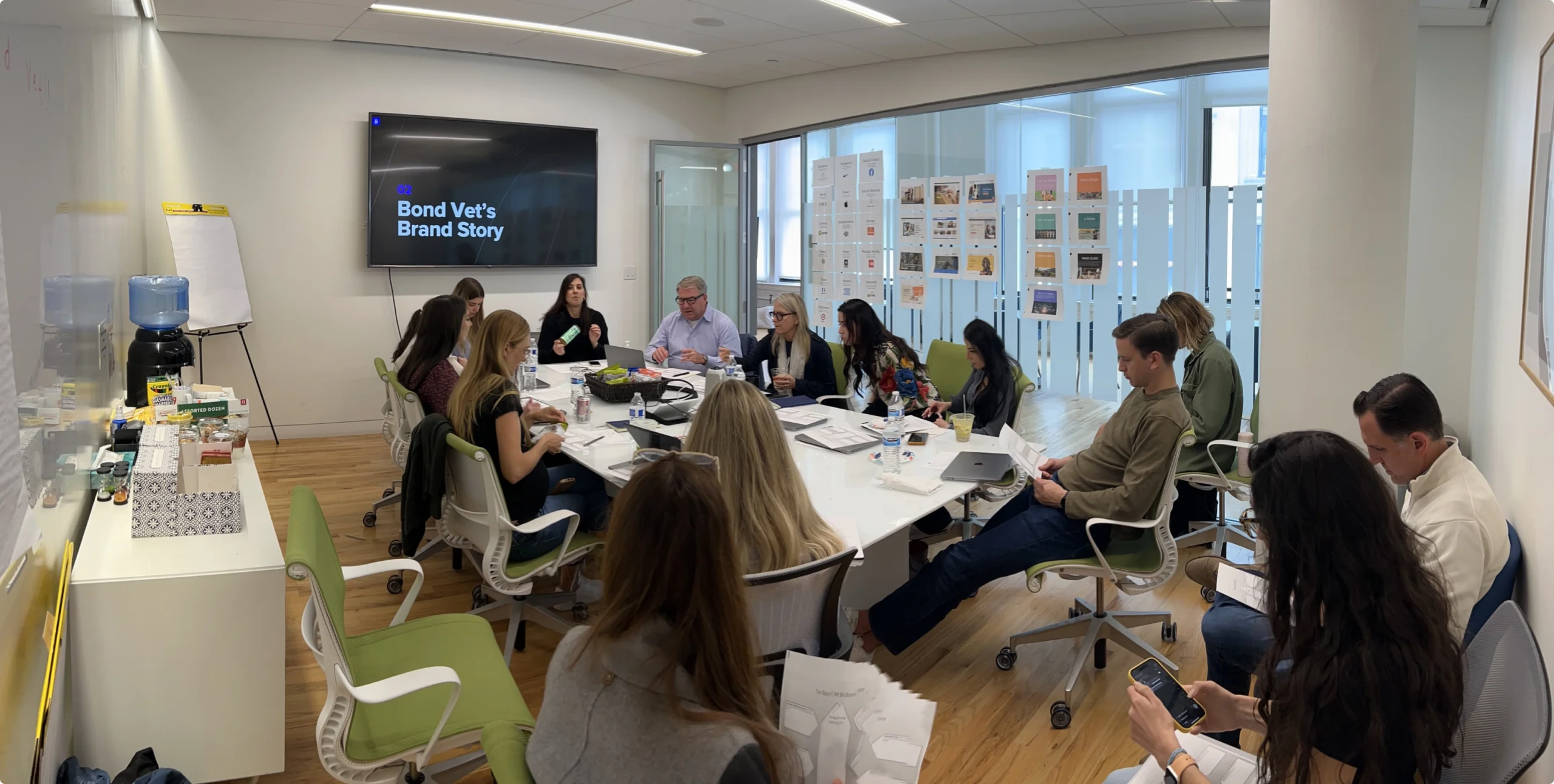 A group of Bond Vet team members and strategists gathered around a conference table during a brand strategy workshop, with a screen reading “Bond Vet’s Brand Story” in the background and brand materials on the walls.